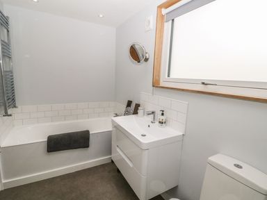 A bathroom with a bathtub towel sink mirror window and toilet at Forest Lodge in Newborough
