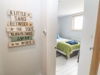 A hallway with a wooden sign on the wall and a partially open door leading to a bedroom with a bed covered with a green blanket and blue towels at Forest Lodge in Newborough