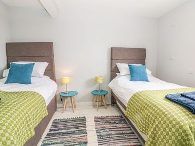 A bedroom with two single beds each with blue pillows and green throws and two small blue bedside tables with lamps at Forest Lodge in Newborough
