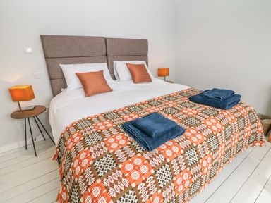 A bedroom with a double bed with a patterned orange and brown blanket and two bedside tables with lamps at Forest Lodge in Newborough