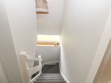 A staircase with grey carpet and white walls a small window with star decorations and a woven hanging light at Forest Lodge in Newborough