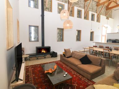A living room with a fireplace two brown sofas a red rug and a dining area with a wooden table and chairs at Tithe Barn in Capel Mawr near Malltraeth