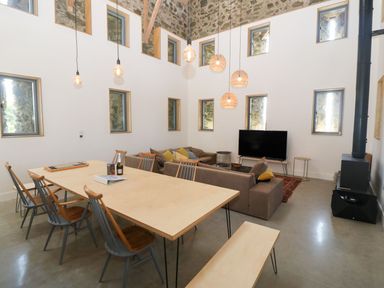 A dining area with a wooden table and chairs next to a living room with sofas and a television at Tithe Barn in Capel Mawr near Malltraeth