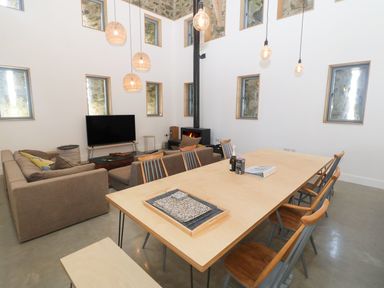 A living and dining area with a wooden table and chairs a sofa a television and a wood burning stove at Tithe Barn in Capel Mawr near Malltraeth