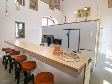 A kitchen with a long wooden counter and brown bar stools at Tithe Barn in Capel Mawr near Malltraeth