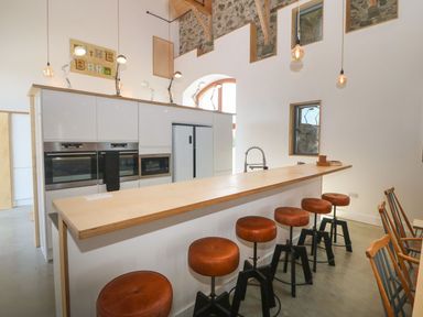 A kitchen with a long wooden counter and six brown stools at Tithe Barn in Capel Mawr near Malltraeth