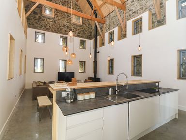 A kitchen with a sink and countertop overlooking a living area with a sofa and television at Tithe Barn in Capel Mawr near Malltraeth