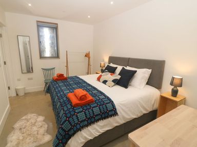 A bedroom with a double bed with pillows and blankets bedside tables with lamps a blue chair and a small rug on the floor at Tithe Barn Capel Mawr near Malltraeth