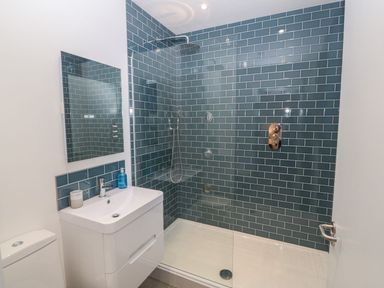 A bathroom with a white sink and vanity mirror and a walk in shower with blue tile walls at Tithe Barn in Capel Mawr near Malltraeth