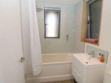 A bathroom with bathtub shower combo a white sink and a mirror with folded towels at Tithe Barn in Capel Mawr near Malltraeth