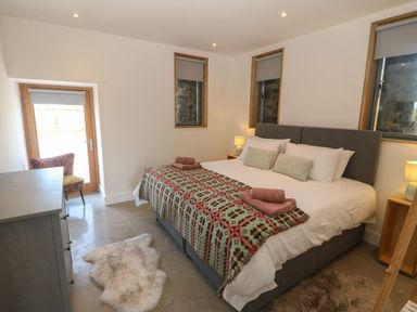 A bedroom with a large bed bedside tables lamps a dresser a chair and two windows at Tithe Barn in Capel Mawr near Malltraeth