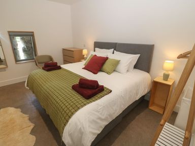 A bedroom with a double bed with green and red cushions and folded towels at Tithe Barn in Capel Mawr near Malltraeth