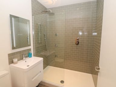 A bathroom with a sink, mirror, and a walk-in shower with green tiled walls at Tithe Barn in Capel Mawr near Malltraeth