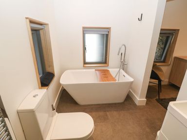 A bathroom with a toilet a freestanding bathtub and two windows at Tithe Barn in Capel Mawr near Malltraeth