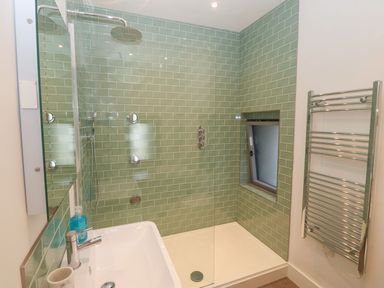 A bathroom with a green tiled walk-in shower a white sink and a chrome towel rail at Tithe Barn in Capel Mawr near Malltraeth