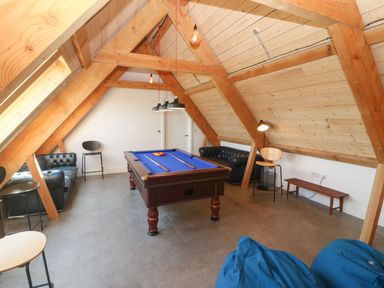 A game room with a pool table two sofas chairs and bean bags under a wooden vaulted ceiling at Tithe Barn in Capel Mawr near Malltraeth