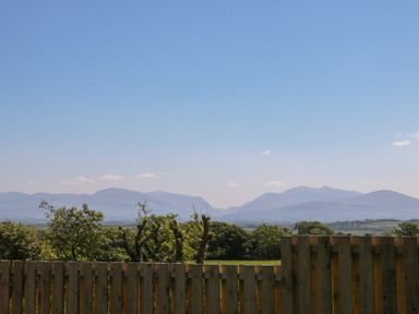 A wooden fence with trees and mountains in the background at Tithe Barn in Capel Mawr near Malltraeth
