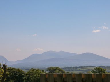 A landscape with trees, fields, and mountains in the background at Tithe Barn in Capel Mawr near Malltraeth