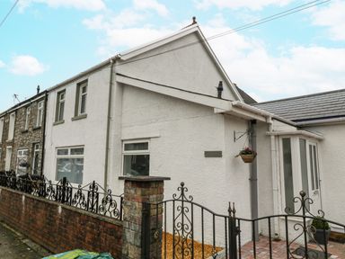 A white exterior house with an iron gate and brick wall a hanging flower basket and paved entrance at Meillion in Hirwaun