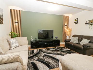 A living room with a beige sofa a brown sofa a black TV stand and a patterned rug at Meillion in Hirwaun