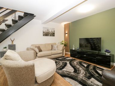 A living room with beige sofas a patterned rug a black television stand and a staircase at Meillion in Hirwaun