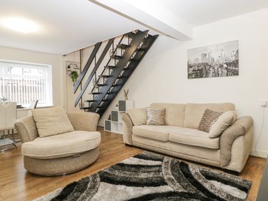 A living room with two beige sofas a black metal staircase and a patterned rug at Meillion in Hirwaun