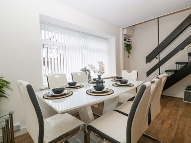A dining room with a glass table set for six near a window and stairs at Meillion in Hirwaun
