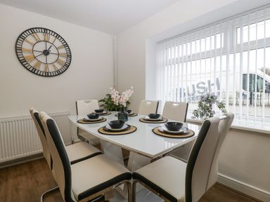 A dining room with a rectangular table set for six beside a window with vertical blinds at Meillion in Hirwaun