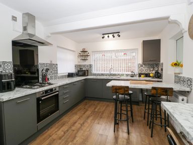 A kitchen with grey cabinets wooden stools marble countertops and patterned tile backsplash at Meillion in Hirwaun
