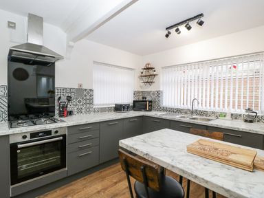A kitchen with marble countertops grey cabinets a gas stove an oven a microwave two sinks and wooden chairs at Meillion in Hirwaun
