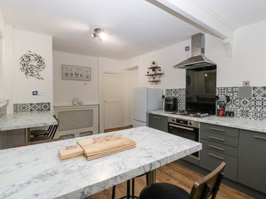 A kitchen with marble countertops a stove a refrigerator and stools at Meillion in Hirwaun