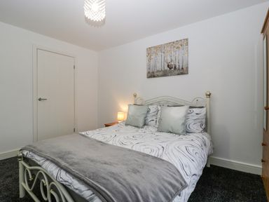 A bedroom with a double bed two pillows a bedside table with a lamp a wardrobe and a painting above the bed at Meillion in Hirwaun