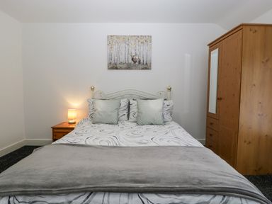 A bedroom with a bed with patterned bedding and pillows a bedside table with a lamp and a wooden wardrobe at Meillion in Hirwaun