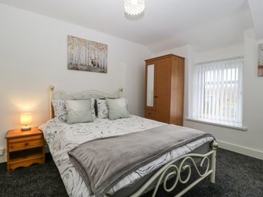 A bedroom with a double bed bedside table with a lamp wooden wardrobe and window with blinds at Meillion in Hirwaun