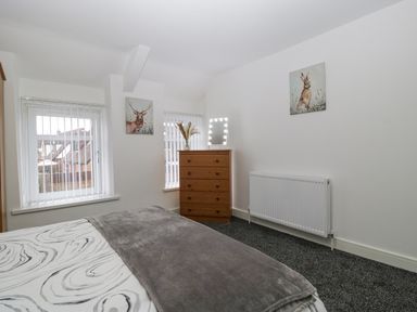 A bedroom with a bed, a wooden chest of drawers, two windows with vertical blinds, and animal paintings on the walls at Meillion in Hirwaun