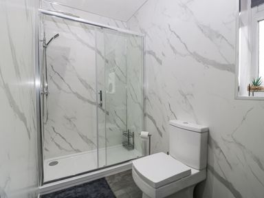 A bathroom with a glass shower enclosure and a white toilet with marble-patterned walls at Meillion in Hirwaun