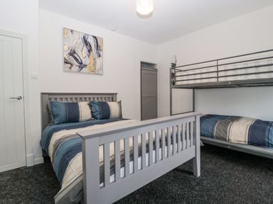 A bedroom with a double bed and a metal bunk bed with striped bedding at Meillion in Hirwaun