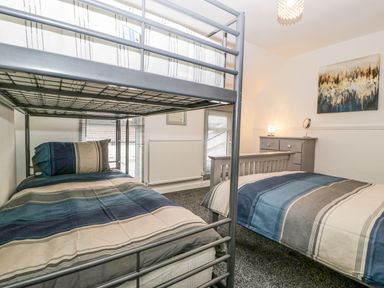 A bedroom with a metal bunk bed and a wooden bed with blue striped bedding at Meillion in Hirwaun