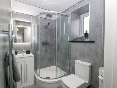 A bathroom with a curved glass shower enclosure a white sink cabinet a toilet a towel rail and a small window with a plant at Meillion in Hirwaun