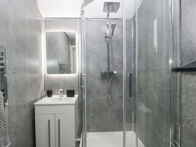 A bathroom with a shower enclosure a white sink cabinet a lit mirror and a towel rail at Meillion in Hirwaun