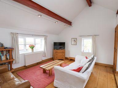 A living room with a white sofa red cushions wooden coffee table and television at The Barn - Poplar Farm in Lower Dunsforth near Boroughbridge