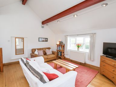 A living room with sofas, a wooden coffee table, a bookshelf, a TV on a wooden dresser, and a window with curtains at The Barn - Poplar Farm in Lower Dunsforth near Boroughbridge