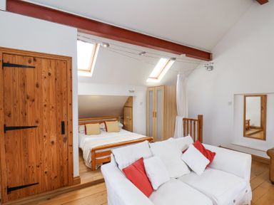 A bedroom with a wooden bed a white sofa with red and white cushions a wooden wardrobe and two skylight windows at The Barn - Poplar Farm in Lower Dunsforth near Boroughbridge