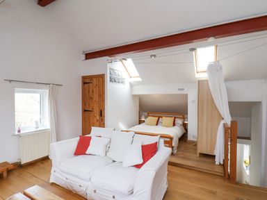 A white sofa with pillows in front of a bed under skylights in a room with wooden floors and a wooden door at The Barn - Poplar Farm in Lower Dunsforth near Boroughbridge