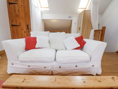 A white sofa with red and white pillows in a room with wooden floors and doors at The Barn - Poplar Farm in Lower Dunsforth near Boroughbridge