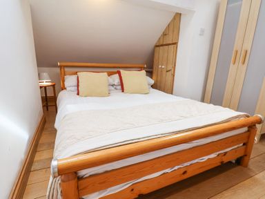 A bedroom with a wooden bed with white bedding and two yellow pillows a wooden wardrobe and a small wooden side table with a lamp at The Barn - Poplar Farm in Lower Dunsforth near Boroughbridge