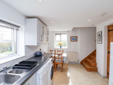 A kitchen with a sink, countertop, washing machine, dining table, chairs, stairs, and windows at The Barn - Poplar Farm in Lower Dunsforth near Boroughbridge