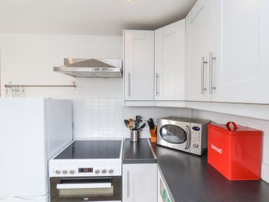 A kitchen with white cabinets a stove a microwave and a red bread box at The Barn - Poplar Farm in Lower Dunsforth near Boroughbridge