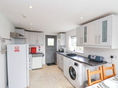 A kitchen with white cabinets appliances a gray door and a dining table with wooden chairs at The Barn - Poplar Farm in Lower Dunsforth near Boroughbridge