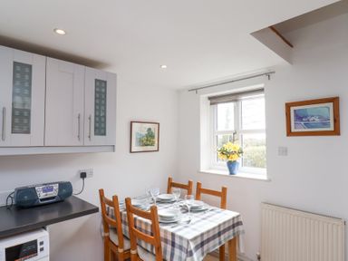 A dining area with a table set for four next to a window with flowers on the sill at The Barn - Poplar Farm in Lower Dunsforth near Boroughbridge